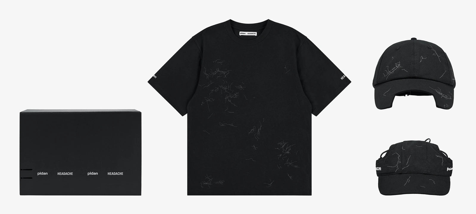 The full set laid out on grey: the black gift box, the tee, the cap and the cat cap